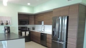 A modern kitchen with stainless steel appliances, wooden cabinets, and a white countertop. - Blue Maho Sxm (Sint Maarten)