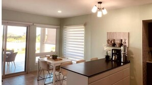 A modern kitchen with a central island, a dining area with a table and chairs, and a view of the outdoors through large windows. - Blue Maho Sxm (Sint Maarten)
