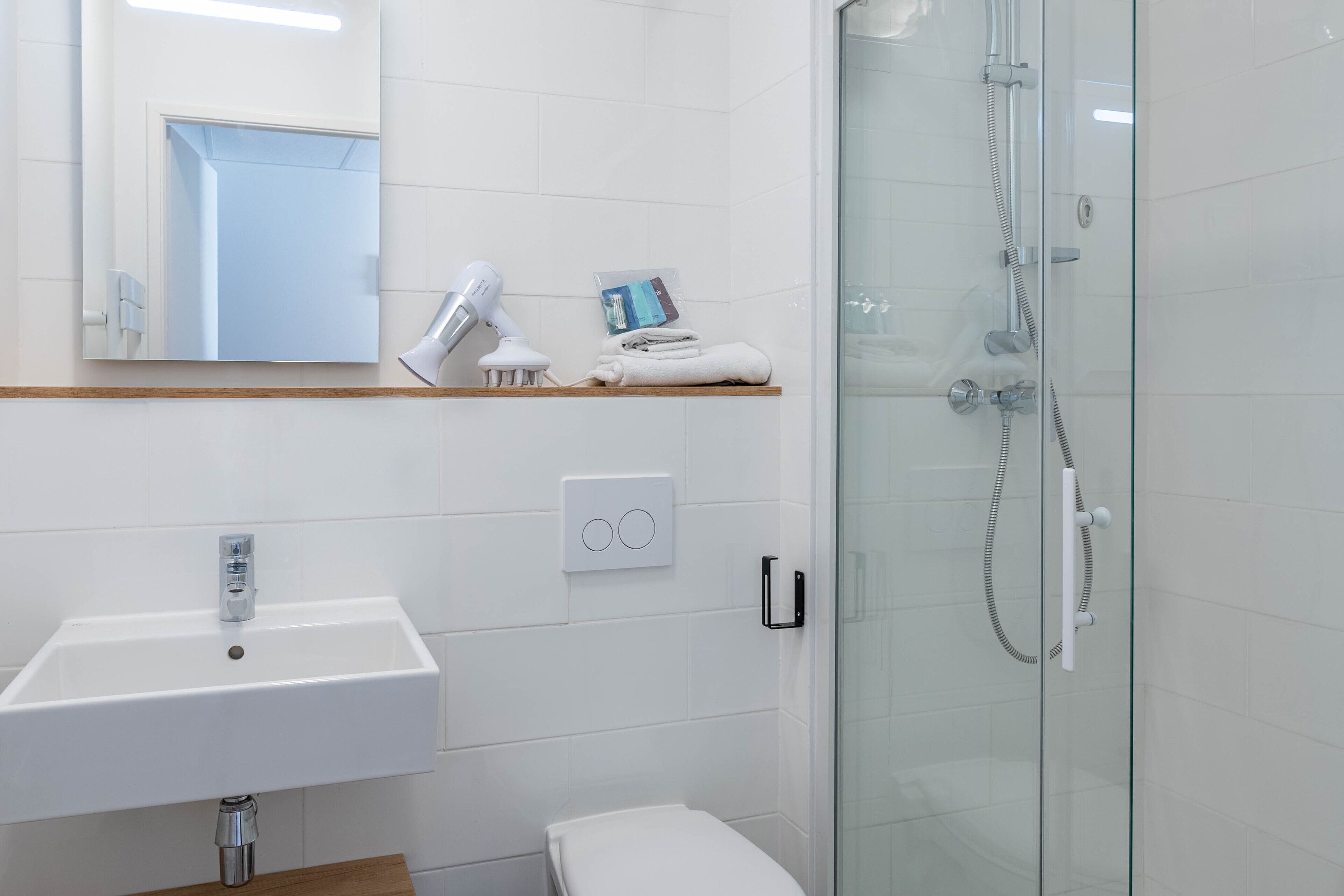 Un baño moderno con un lavabo blanco, una cabina de ducha de vidrio y un espejo sobre el lavabo.