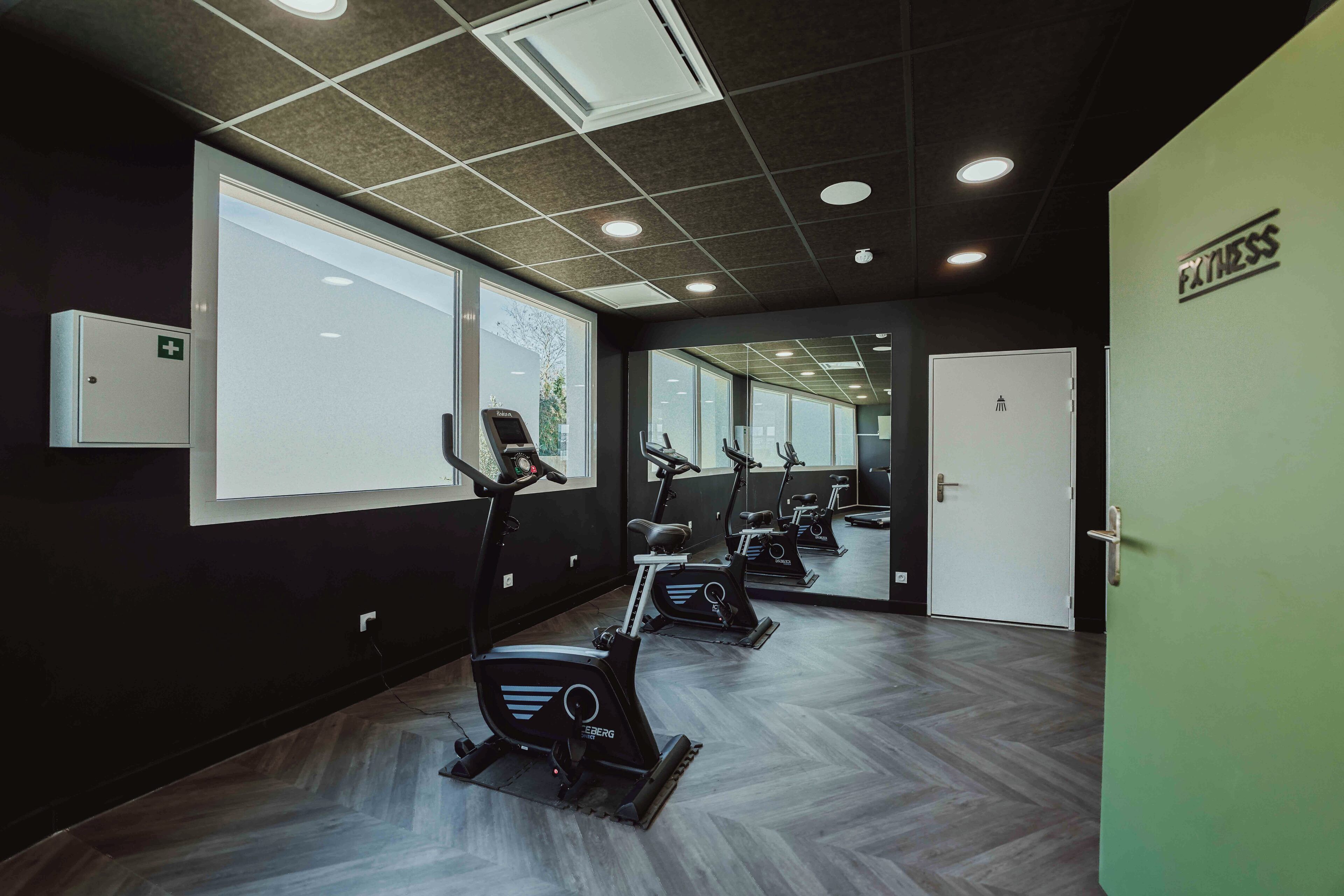 Ein Fitnessraum mit Ergometer, einer Spiegelwand und einer Tür mit der Aufschrift 'EXERCISE'.