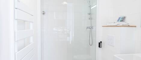 Un baño moderno con ducha envuelta en vidrio, inodoro blanco y lavamanos blanco.