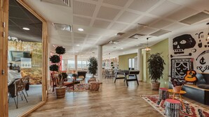 A spacious living area with wooden flooring, a large window, and a dining area with chairs and tables. - UXCO Kabane Montpellier (Lattes)