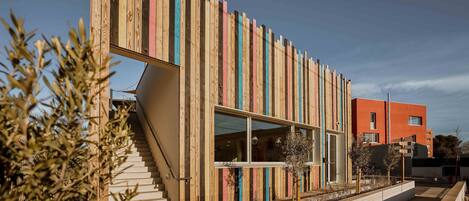 Un edificio moderno con fachada de madera, una escalera y un camino con macetas.