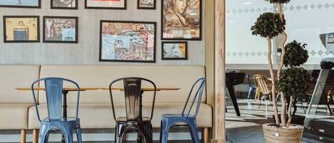 Een eethoek met een houten tafel en blauwe stoelen, een potplant en kunstwerken in lijsten aan de muur.