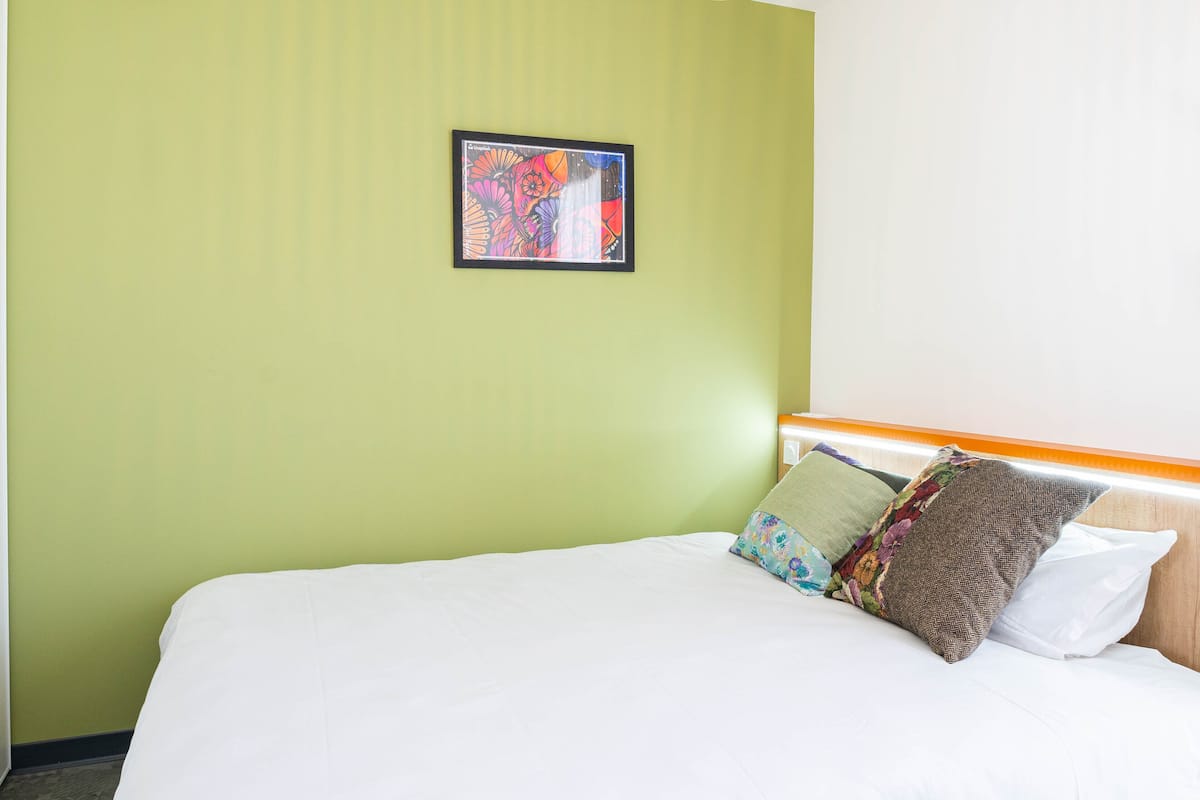 A hotel room with a bed, pillows, and a framed artwork on the wall.