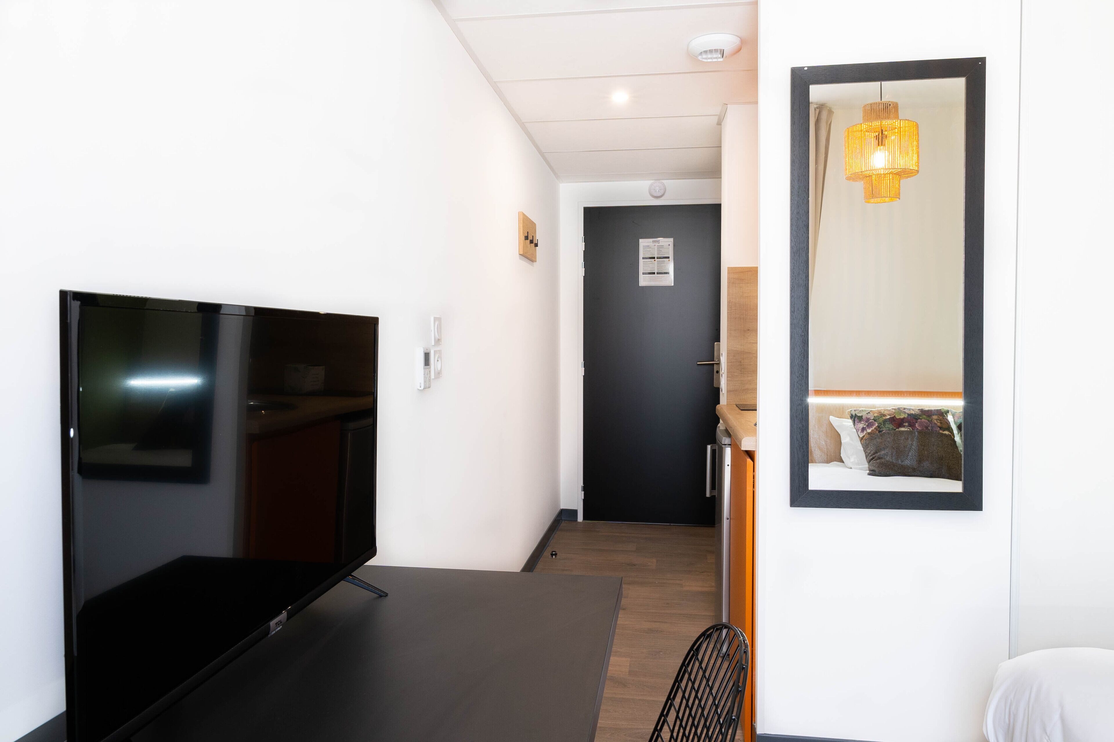 Een moderne hotelkamer met een flatscreen televisie, een houten deur, een spiegel en een hangende lamp.