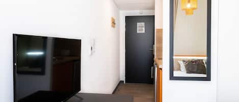 A modern hotel room with a flat-screen TV, a wooden door, a mirror, and a hanging light fixture.
