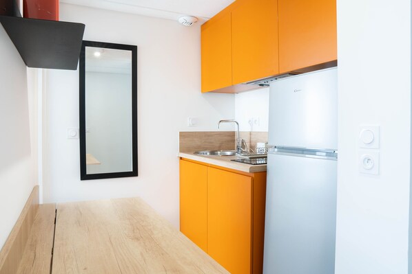 Una cocina compacta con un refrigerador blanco, armarios color naranja, una encimera de madera y un espejo con marco negro.