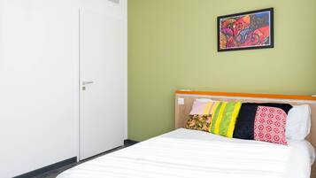A hotel room with a bed, a door, and a wall with a colorful painting.