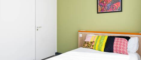 A hotel room with a bed, a door, and a wall with a colorful painting.