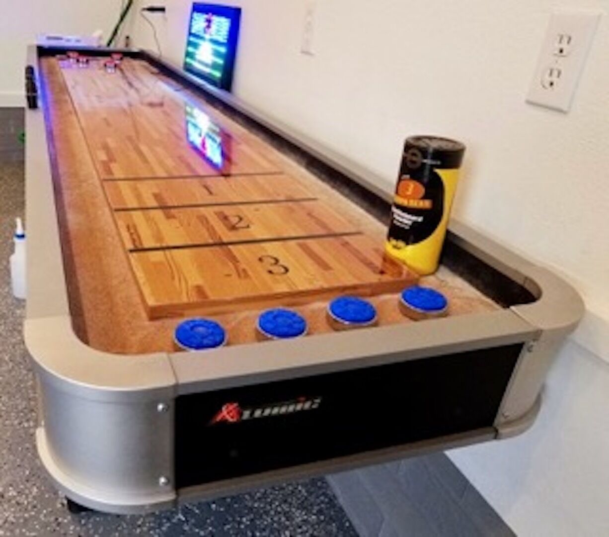 A shuffleboard table with numbered scoring areas and a bottle of lubricant on it.