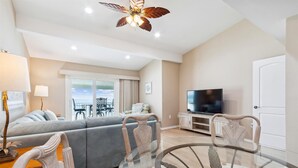 Ein modernes Wohnzimmer mit einer Couch, einem Glastisch, einem Fernseher und einem Deckenventilator.