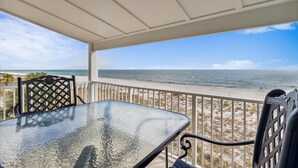 Überdachte Terrasse mit Glastisch und Metallstühlen mit Blick auf einen Strand.