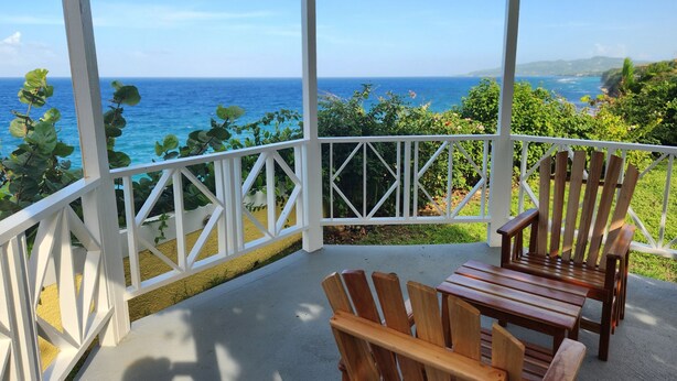 A covered outdoor area with wooden chairs and a view of the ocean. - Oasis Palms Luxury Villa (Tower Isle)