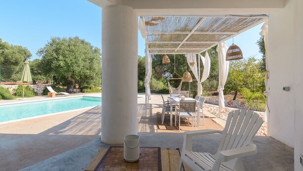 A covered outdoor seating area with a pool, white chairs, and a table. - Trullo Chiara con piscina by Wonderful Italy (Ostuni)