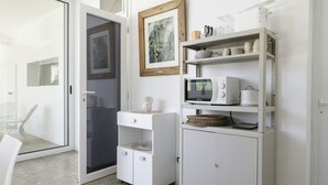 A kitchen with white cabinetry, a microwave, and a coffee maker. There is a framed picture on the wall and a chair in the corner. - Trullo Chiara con piscina by Wonderful Italy (Ostuni)