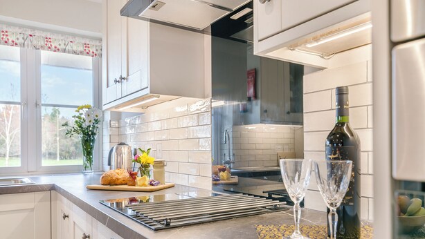 Een moderne keuken met witte kasten, een roestvrijstalen afzuigkap, een fles wijn en twee wijnglazen op het aanrecht.