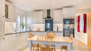 Een moderne keuken met witte kasten, een centraal eiland met stoelen, een ingebouwde kookplaat en een grote afzuigkap.