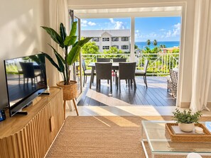 A modern living room with a TV, a large plant, and a dining area with chairs and a table. - Sandbox Villa Stylish 2-bedroom on West Coast in St. James - steps to beach (Weston)