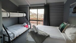 Une chambre d’hôtel avec des lits superposés, une grande fenêtre donnant sur un beau paysage et un luminaire au plafond.