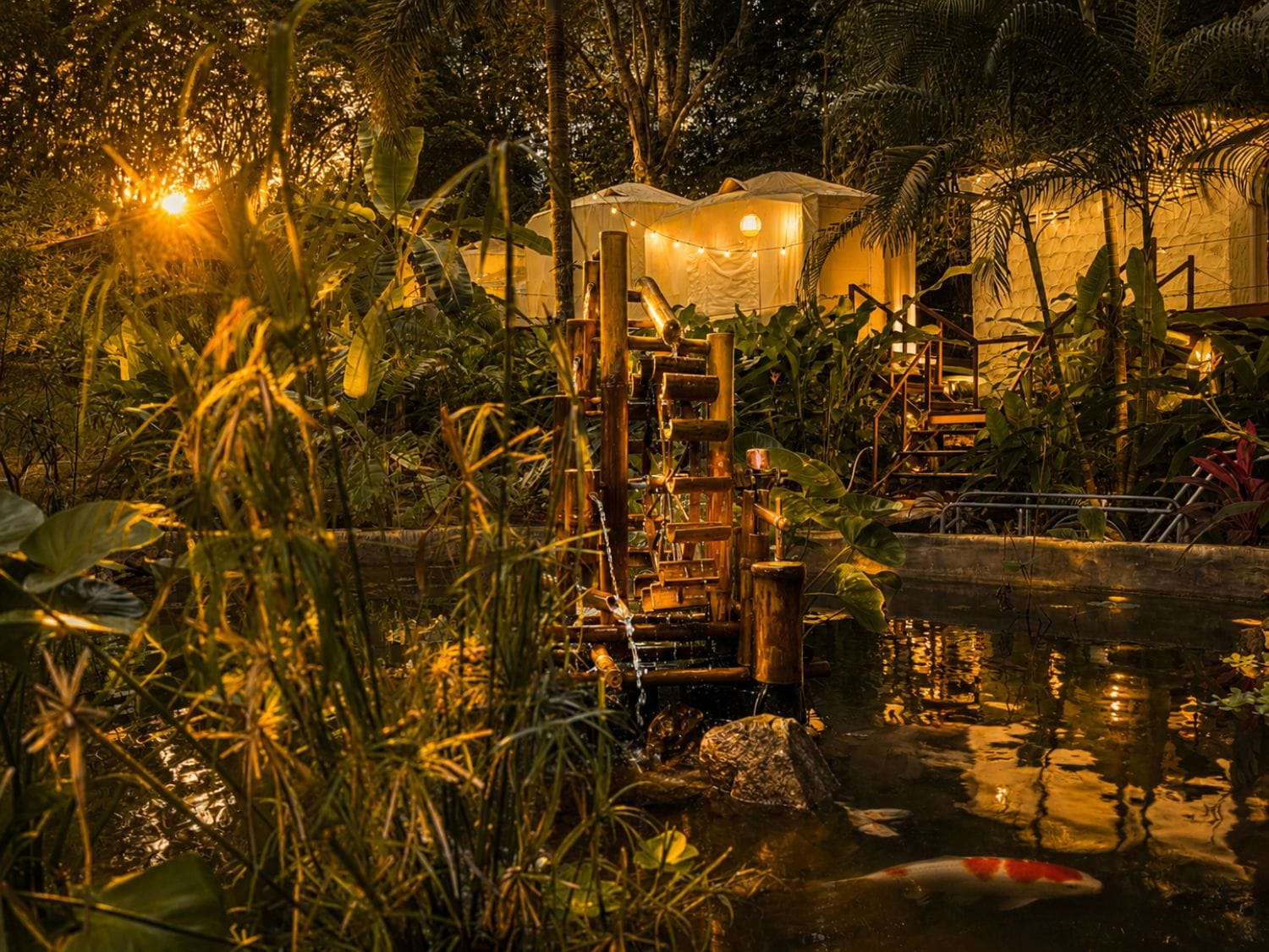 A tranquil garden with a koi pond, bamboo structures, and a tent-like building.