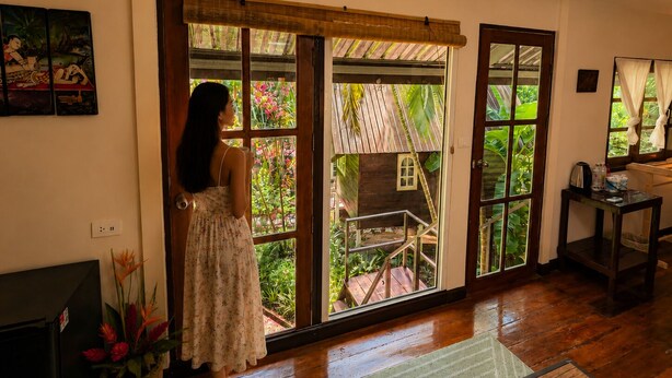 A room with a wooden floor, a large sliding glass door, a small wooden structure outside, and a television on the left. - Vanara Bungalows  (Ko Chang)