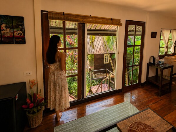 A room with a wooden floor, a large sliding glass door, a small wooden structure outside, and a television on the left. - Vanara Bungalows  (Ko Chang)
