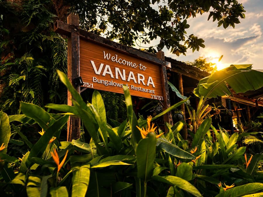 A wooden sign with 'Welcome to VANARA Bungalows & Restaurant' written on it, surrounded by lush greenery.