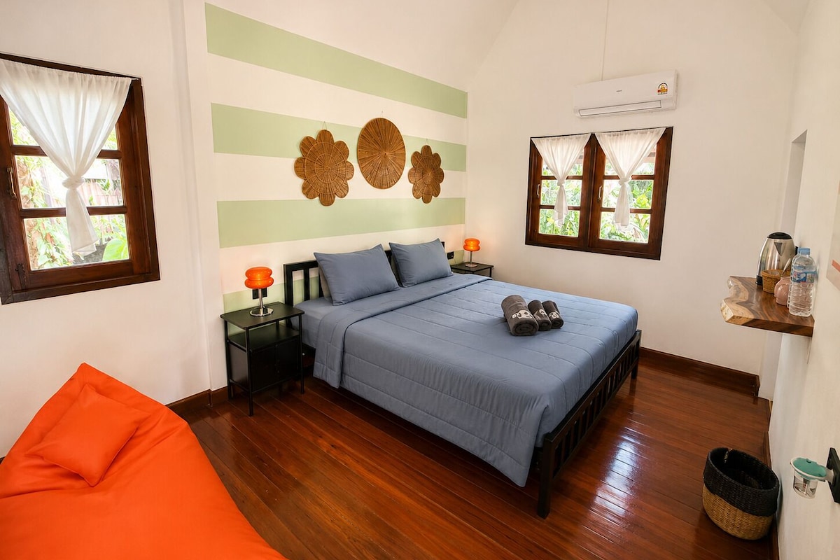Un dormitorio con cama, mesitas de noche, una silla y decoración en la pared.