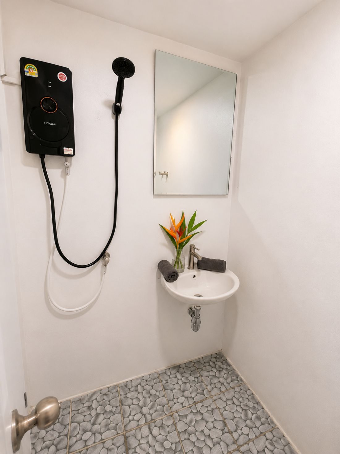 Ein Badezimmer mit Duschbrause, Waschbecken, Spiegel und einer Tür mit Griff.