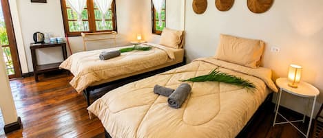 Een kamer met twee bedden, een klein tafeltje, een stoel en een raam met gordijnen.