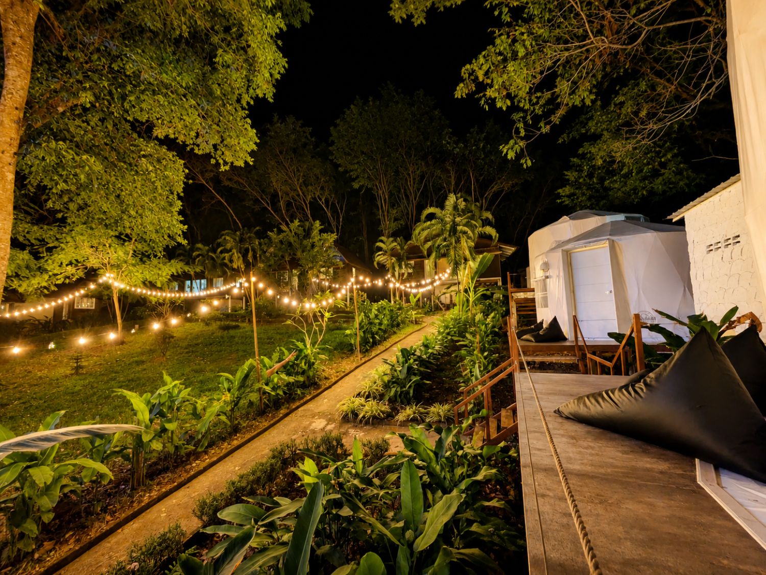 A nighttime outdoor area with a pathway, string lights, and a white structure.