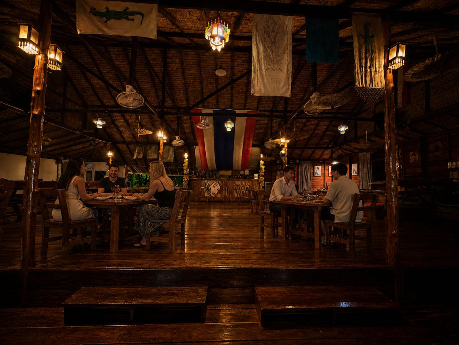 A rustic interior with wooden beams, tables, and benches.