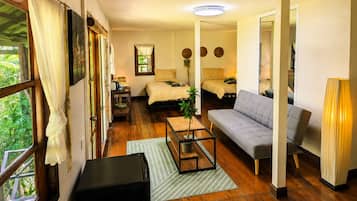 A room with a bed, a sofa, a coffee table, and a lamp. There is a window with curtains, a door, and a mirror.