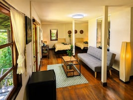 A room with a bed, a sofa, a coffee table, and a lamp. There is a window with curtains, a door, and a mirror.
