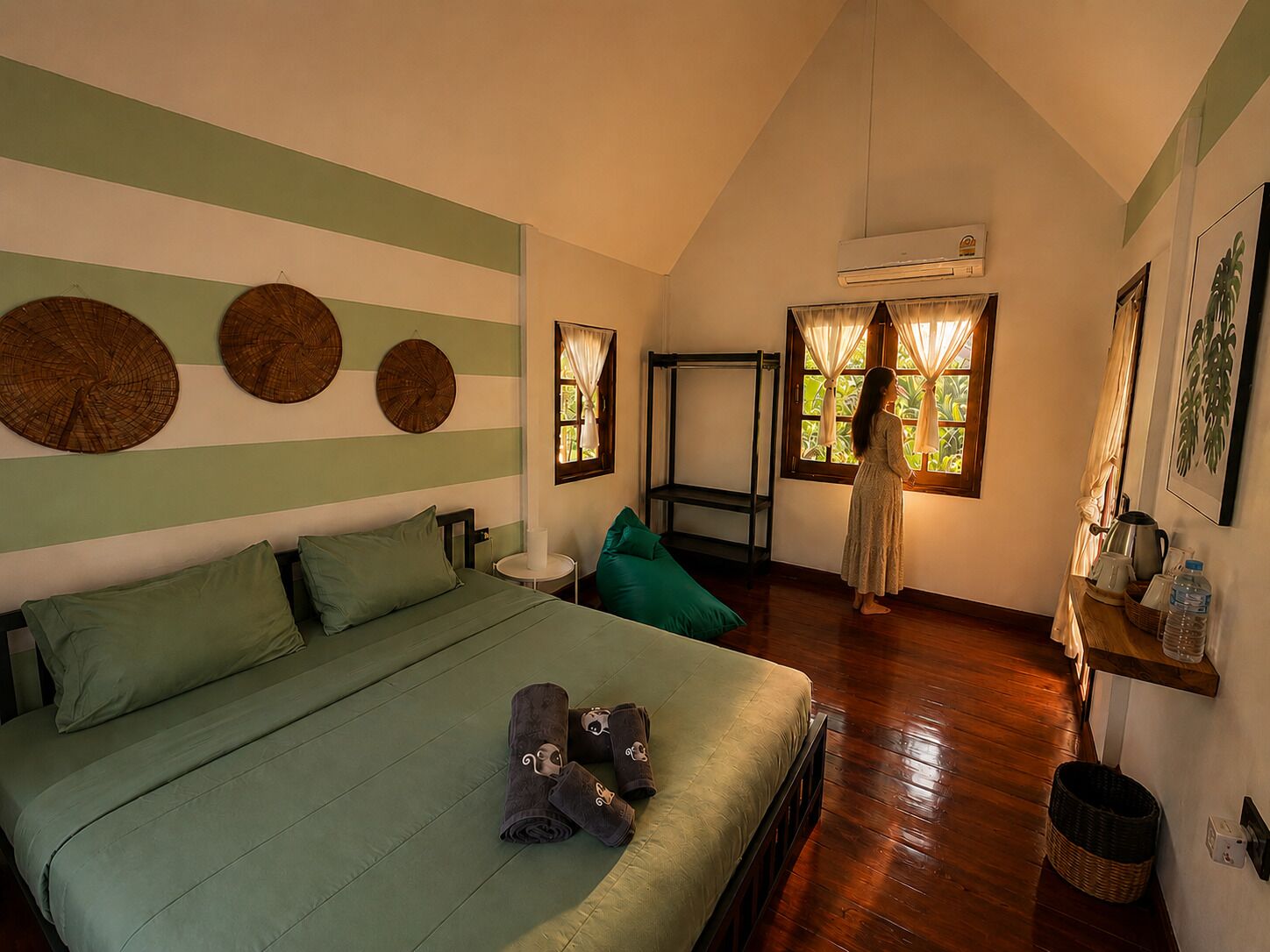 A bedroom with a bed, a standing fan, a window with curtains, and a wall-mounted air conditioner.