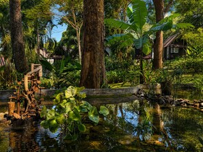 A pond with water lilies, a wooden structure, and a house surrounded by trees. - Vanara Bungalows  (Ko Chang)