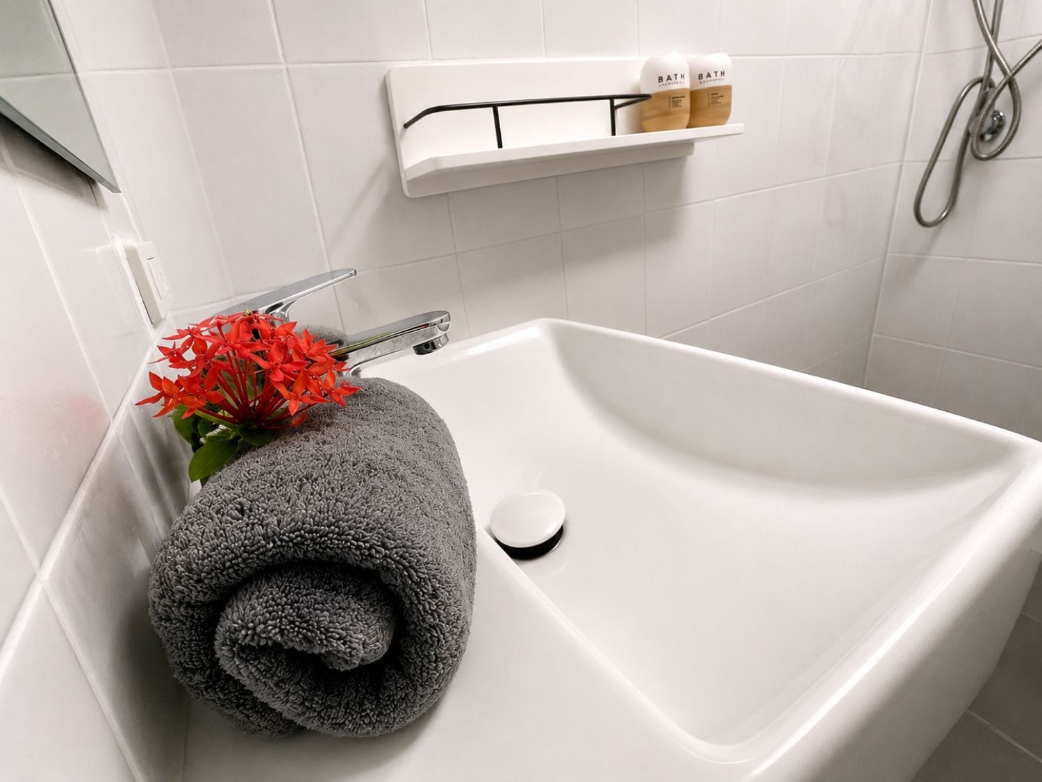 Un baño con un lavamanos blanco, una toalla y una flor.