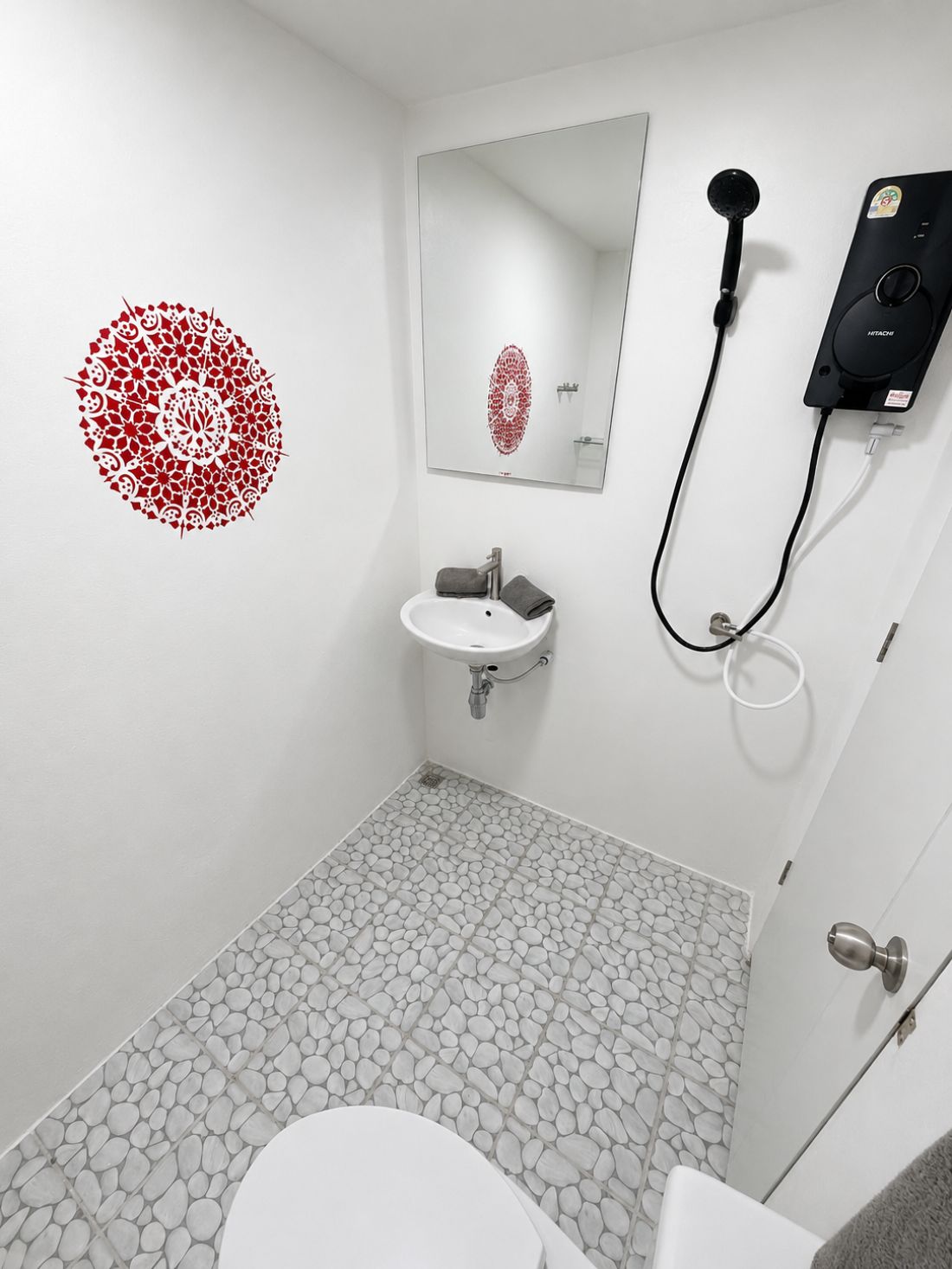 Uma casa de banho com lavatório branco, espelho, chuveiro manual e sanita.