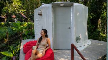 A person sitting on a red bean bag chair in front of a white portable toilet.