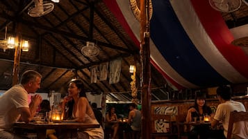 An indoor dining area with wooden tables and chairs, hanging lanterns, and a large flag.