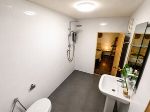 A modern bathroom with a shower, toilet, and sink, featuring white tiles and a glass shelf.