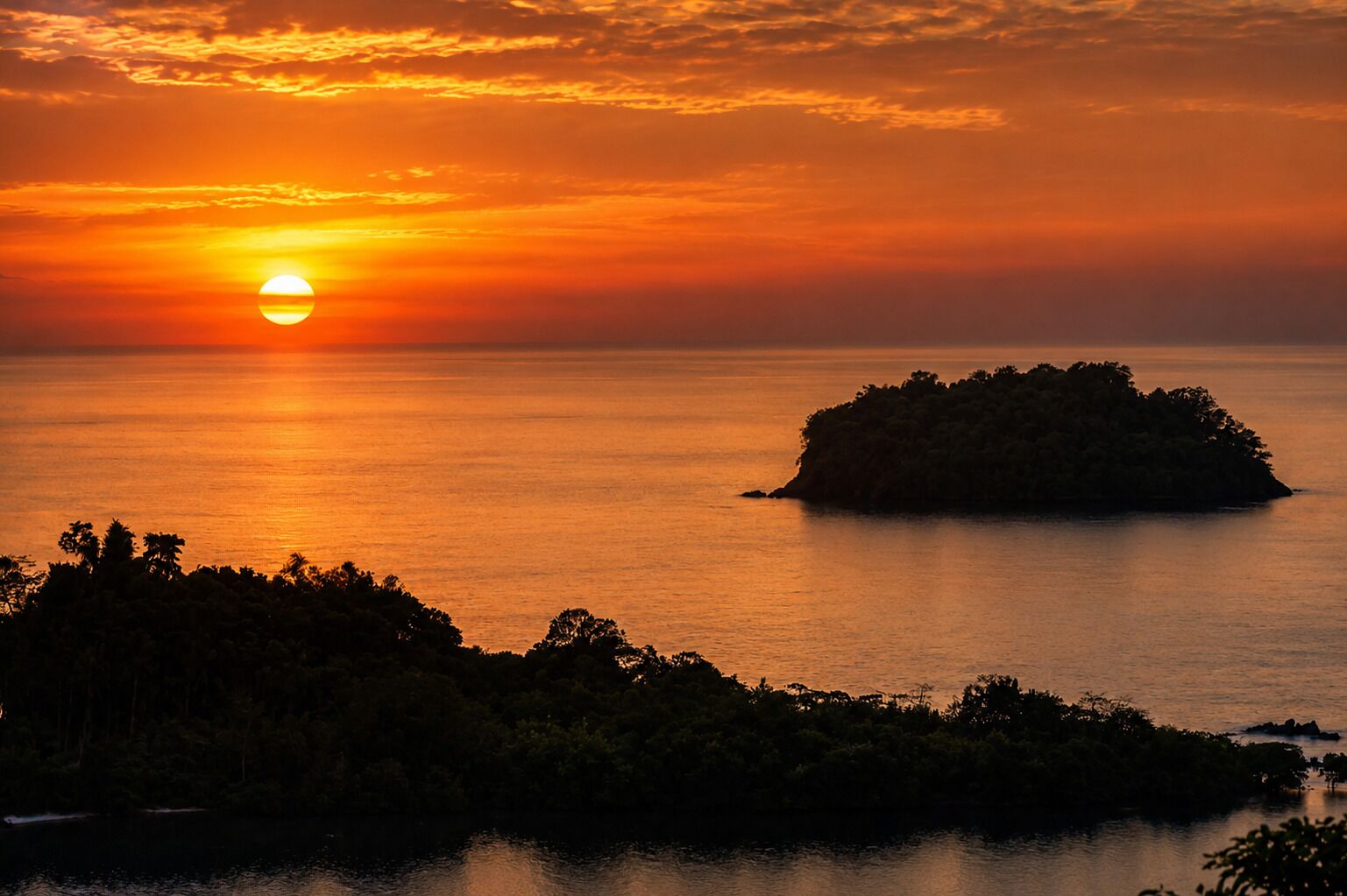 A sunset over a calm sea with a small island in the foreground.