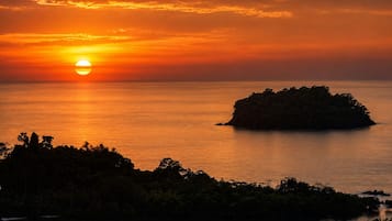A sunset over a calm sea with a small island in the foreground.