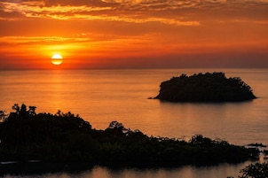 A sunset over a calm sea with a small island in the foreground.
