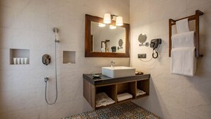 Un baño con un espejo grande, un lavamanos, una ducha, un perchero para toallas y un teléfono.