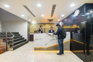 Un hall d’accueil d’hôtel avec un comptoir en marbre, une horloge et un escalier.