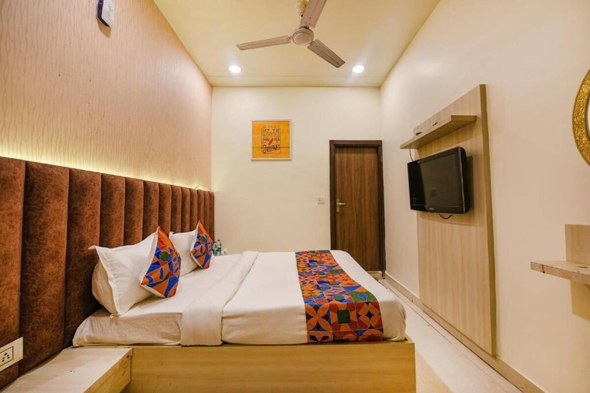 Un dormitorio con cama, ventilador de techo, televisión montada en la pared y una puerta.