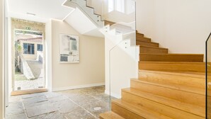 Eine moderne Treppe mit Holzbeschlägen und Glastrennungen, die zu einem Raum mit Steinboden und einer Tür nach draußen führt.