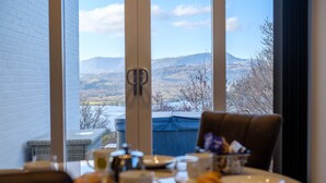 A dining table with a view of mountains through large windows. - Paddock House (Windermere)